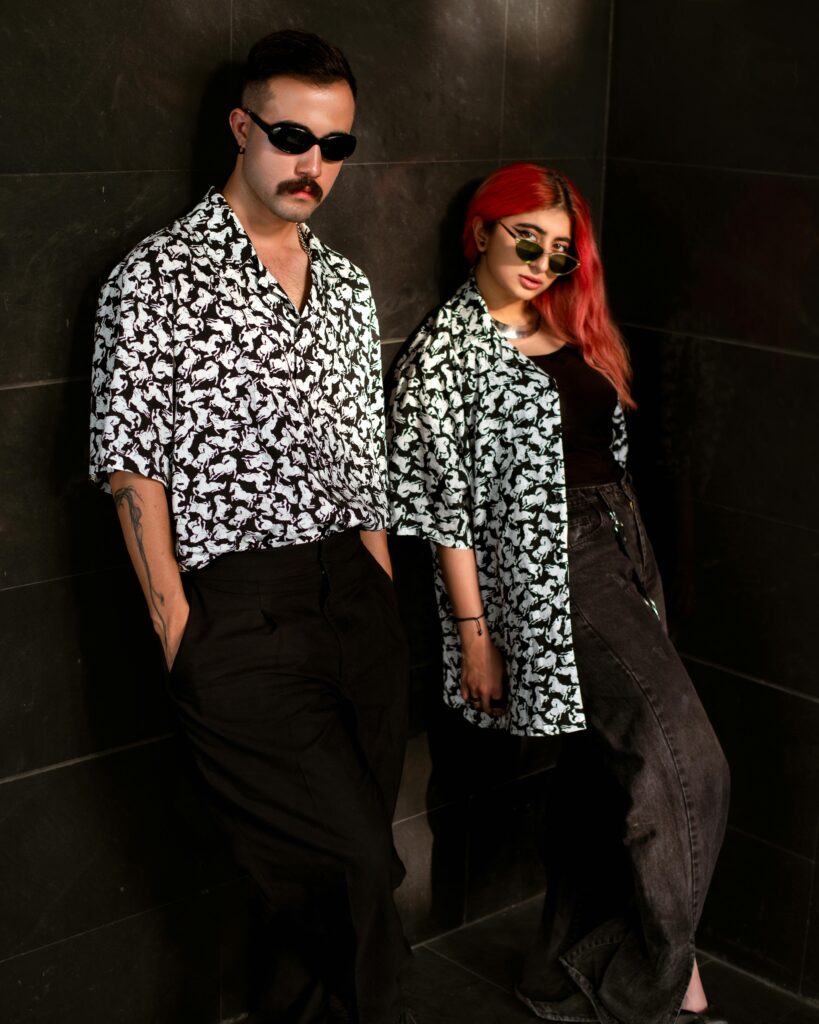 Stylish young adults in sunglasses and matching shirts pose against a wall.